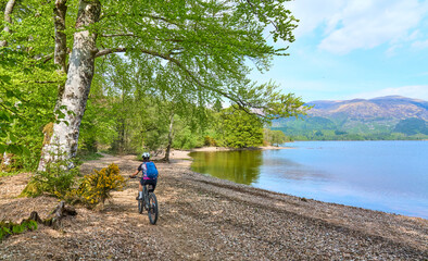 active senior woman riding her electric mountain bike along Loch Lochy, part of the Caledonian...
