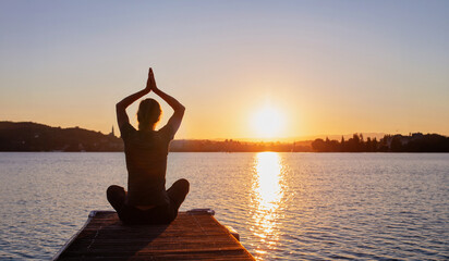 yoga, silhouette of woman doing meditation and breathing exercises on wooden pier near lake, lotus position