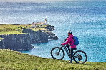 active senior woman riding her electric mountain bike on the cliffs of nest point lighthouse on the...