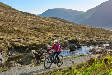 active woman riding her electric mountain bike along the awesome fairy pools on the Isle of Skye in...