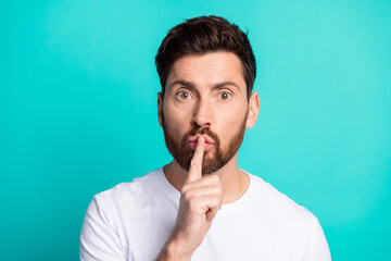 Young man gesturing for silence with his finger on lips against a teal background