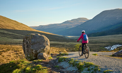 active woman riding her electric mountain bike along the awesome fairy pools on the Isle of Skye in...
