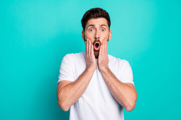 Young man expressing surprise and amazement in casual attire with hand gestures on teal background