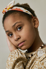 Portrait of a young girl resting her head on her hand, wearing a patterned headband and detailed...