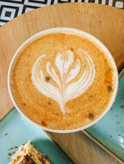 Latte with decorative milk foam on wooden table, dessert in background