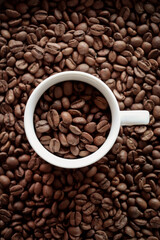 Espresso cup with coffee beans and background full of roasted coffee beans.