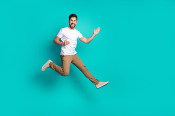 Energetic young man jumping cheerfully against turquoise background in casual attire for...