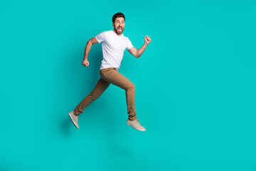 Energetic man jumping in casual style with cheerful expression on a vibrant teal background,...