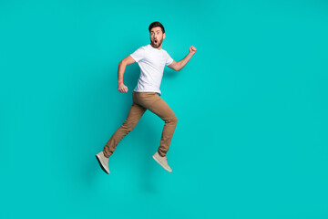 Energetic man leaping against bright turquoise background showcasing casual youthful lifestyle and...