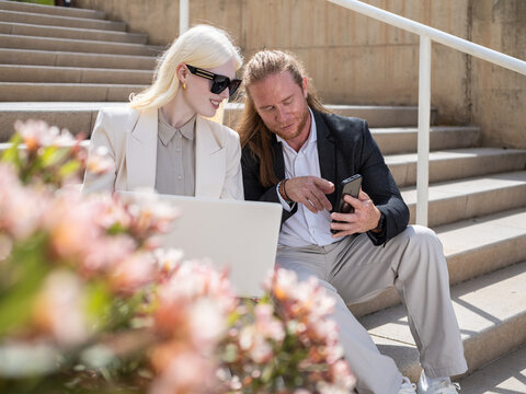 Business people using laptop and smartphone on stairs
