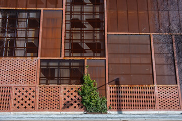 Architectural detail of a ventilated red metal facade with perforations and bricks, combining material texture and geometric rhythm in contemporary urban design