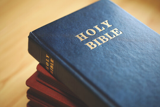 Stack of Holy Bibles with a close-up focus on the top blue Bible. Represents Christian scripture, religious faith, devotion