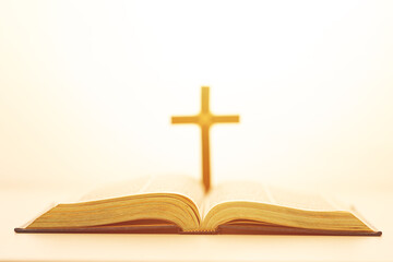 Open Bible with a glowing cross in the background, symbolizing faith, divine guidance, and spiritual enlightenment in warm golden light.