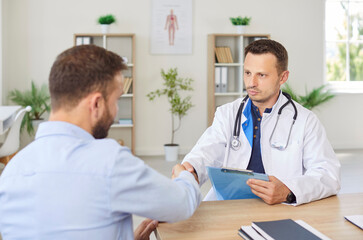 Confident young male doctor therapist in white uniform shaking hands with a man patient sitting at...