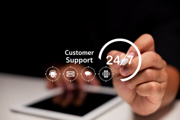 A person interacts with a digital interface displaying 24/7 customer support icons over a tablet,...