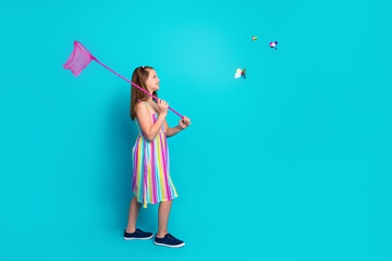 Smiling young girl with butterfly net in colorful dress on turquoise background, enjoying summer...