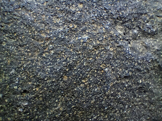 texture of dark volcanic rock with shiny mineral inclusions and rough surface, showing natural...
