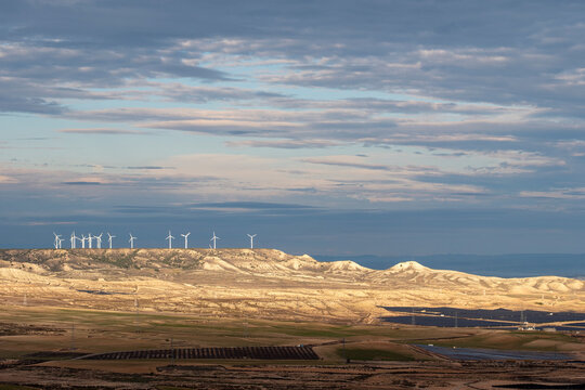 Distant wind farm on sunlit hills with layered skies in Arag&oacute;n, Spain, capturing renewable energy deployment and harmonious integration with natural terrain