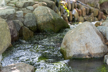 Stream with large stones. A natural stream winds its way through smooth, mossy rocks. The water is clear and moves gently.