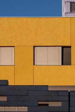 Yellow modern facade with square windows and geometric modules in strong daylight, creating bold architectural color field for background or graphic design purposes