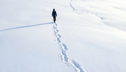 A person walks across a snow-covered field leaving footprints behind.