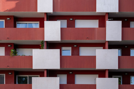 Modern residential facade with alternating red and white balcony modules, viewed frontally as an abstract architectural pattern perfect for graphic and commercial use