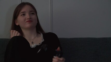 Young teen girl playing video games sitting cross-legged on couch showing intense emotional reactions while immersing herself in digital gameplay with concentrated concentration