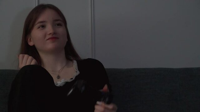 Young teen girl playing video games sitting cross-legged on couch showing intense emotional reactions while immersing herself in digital gameplay with concentrated concentration