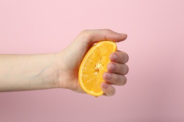 Woman squeezing orange on pink background, closeup
