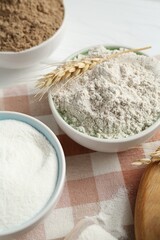 Different types of flour in bowls and spike on table, closeup