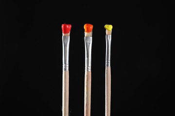 Three brushes with color paints on black background, closeup