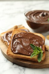 Tasty chocolate spread with mint and hazelnuts on white marble table, closeup