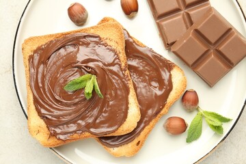 Toasts with tasty chocolate spread, pieces, mint and hazelnuts on light table, top view