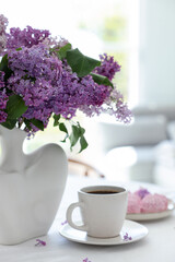 Bouquet of beautiful lilac flowers, coffee and dessert on white table indoors