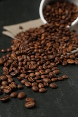 Aromatic coffee beans and overturned cup on black table, closeup