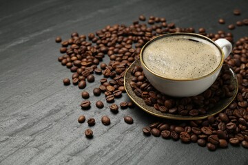 Aromatic coffee in cup and beans on black table, closeup. Space for text