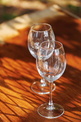 Two empty wine glasses on wooden table in natural sunlight with warm reflections and shadows