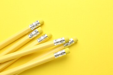 Many graphite pencils with erasers on yellow background, flat lay. Space for text