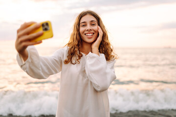 Portrait of young woman with phone in hands takes selfie with the sea in background. Beautiful...