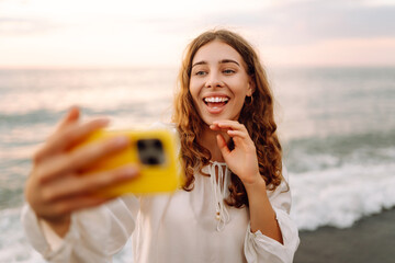 Portrait of young woman with phone in hands takes selfie with the sea in background. Beautiful...