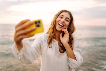 Portrait of young woman with phone in hands takes selfie with the sea in background. Beautiful...