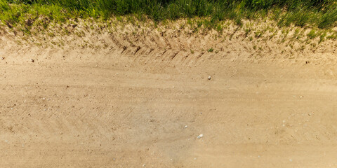 top view of gravel road surface and grass shoulder with tractor tire tracks in countryside