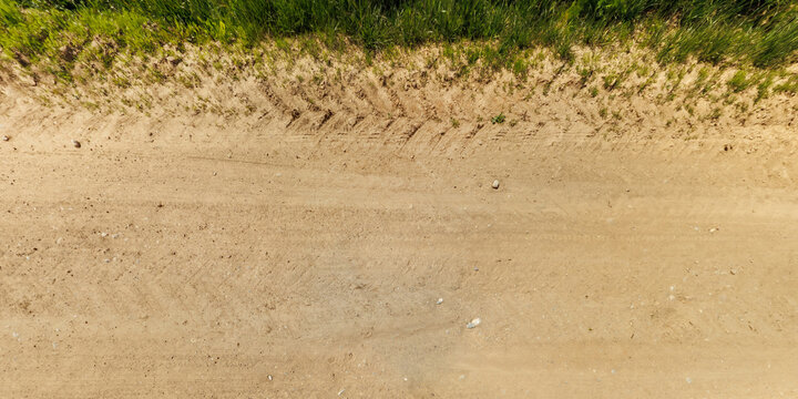 Fototapeta top view of gravel road surface and grass shoulder with tractor tire tracks in countryside