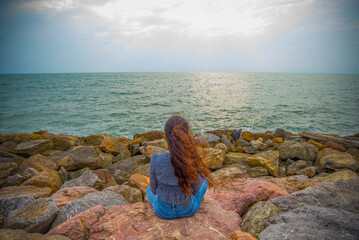 Young woman sitting on the rock and looking at the sea in the evening