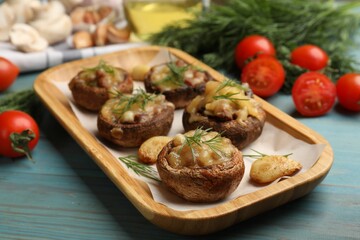Delicious stuffed mushrooms with melted cheese, garlic and dill on light blue wooden table, closeup