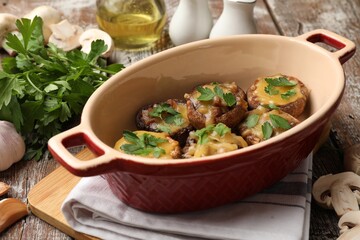 Delicious stuffed mushrooms with melted cheese and parsley in baking dish on color wooden table,...