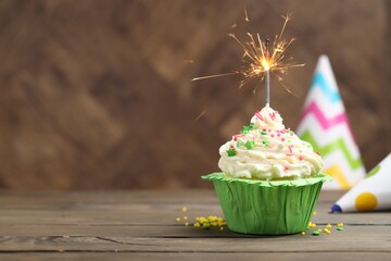 Burning sparkler in cupcake, sprinkles and party hats on wooden table, space for text