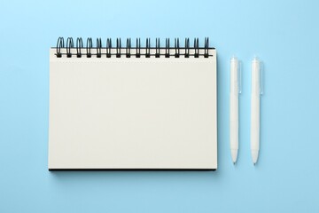 Notebook and pens a on light blue background, flat lay