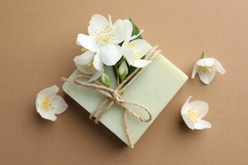 Soap bar and jasmine flowers on light brown background, flat lay