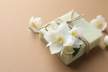 Soap bar and jasmine flowers on light brown background, closeup. Space for text